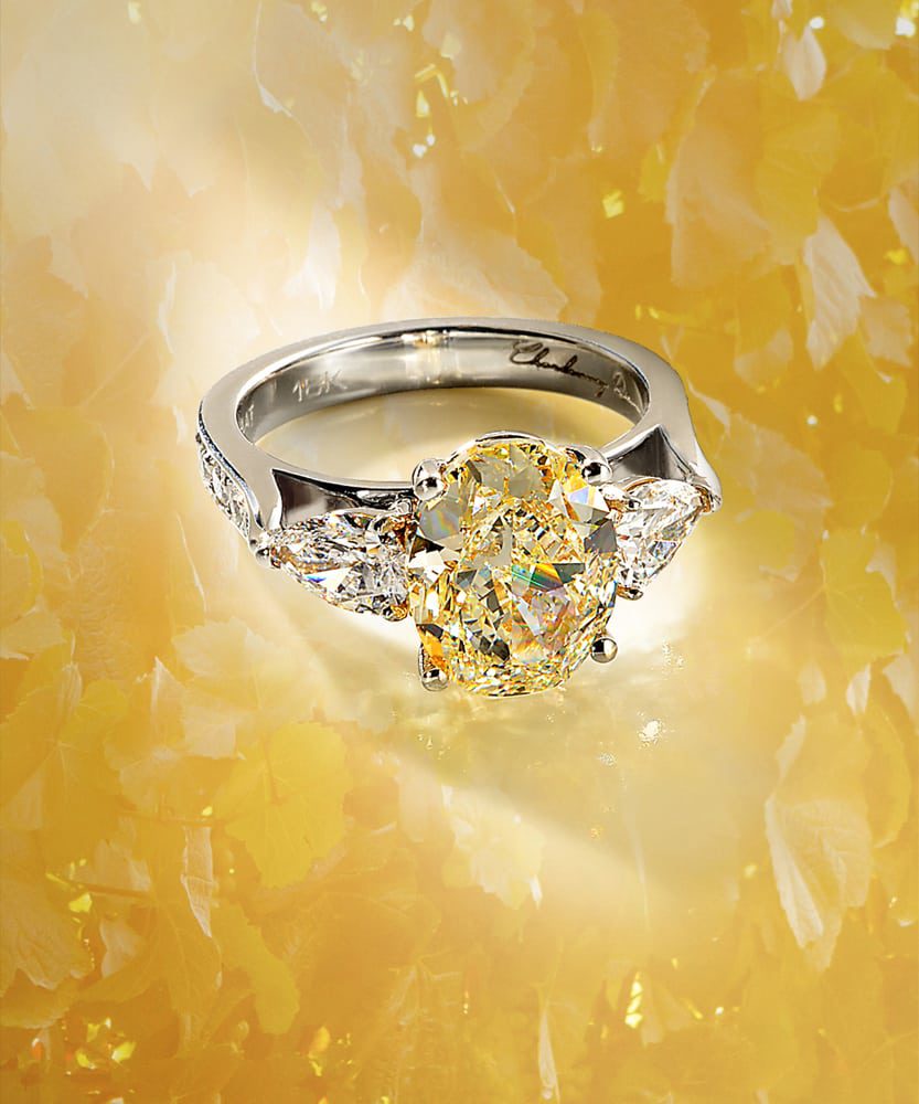 Large oval yellow diamond ring with 18K band and two pear shaped diamonds all on floral looking yellow background Product Photography