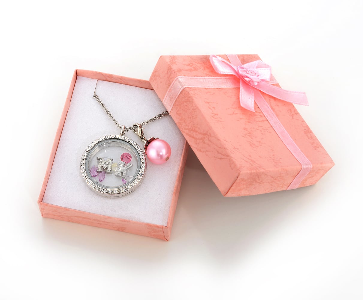 Small Pink gift box with pink ribbon opened holding a silver pendant with letters "M" and "K" inside glass and a pink pearl all on a silver chain. Product Photography