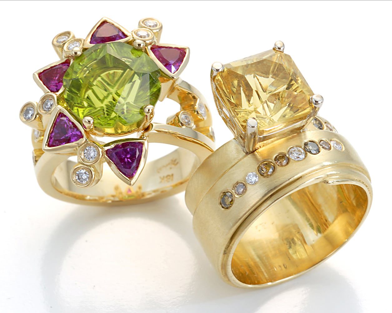 two gold rings standing together. the left one with a star pattern made of a large green stone surrounded by purple stones and diamonds sprinkled. The right one has a large yellow radiant cut stone with brown and white diamonds embedded on band Product Photography