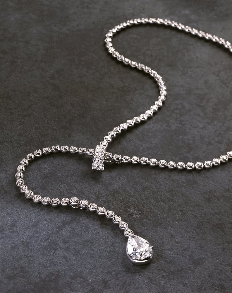 String of diamond adjustable necklace with large pear shaped diamond on end, all on gray slate background