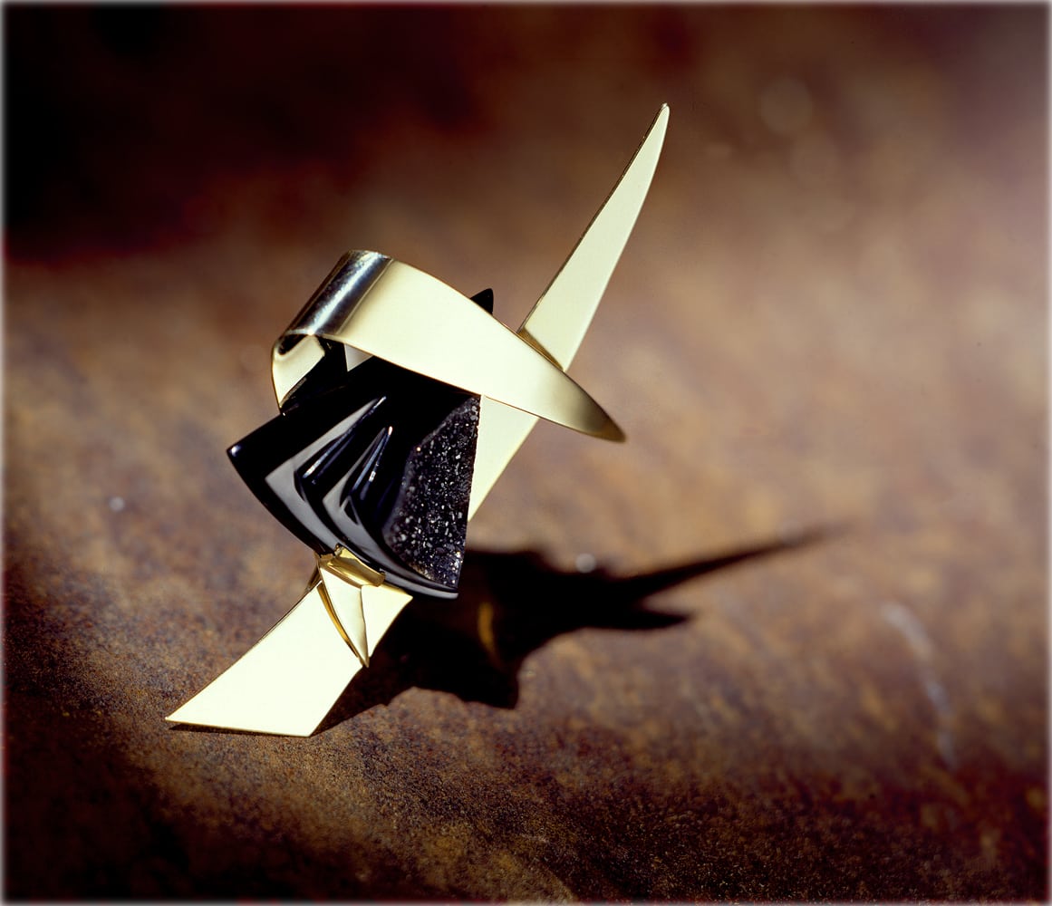 Angular gold and black onyx pin with strong shadow on rusty metal background