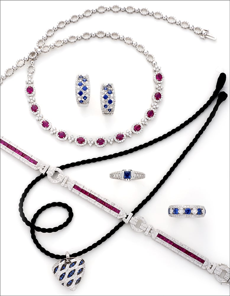 Design Arrangement of ruby necklace, Diamond and ruby bracelet, Sapphire and diamond heart pendant on black cord, and four sapphire and diamond rings on white background