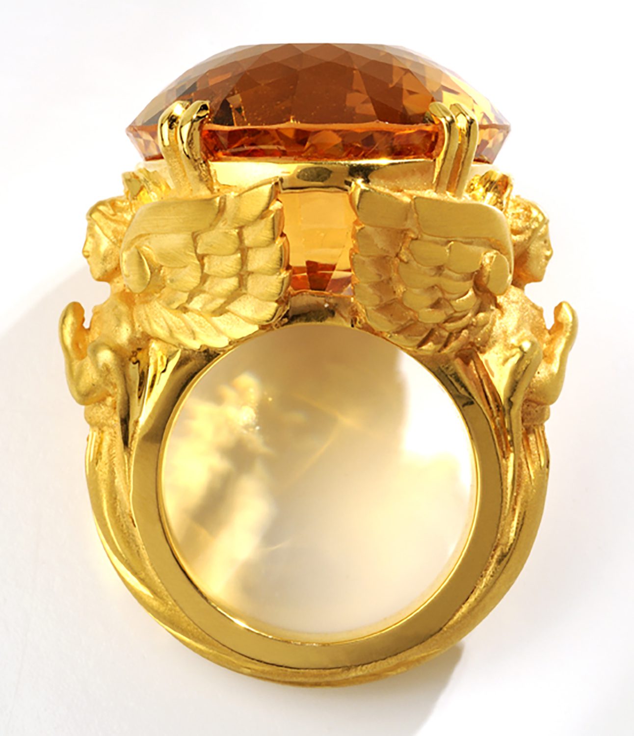Large museum oval topaz mounted on heavy gold ring flanked by twin angel carvings on white background Product Photography