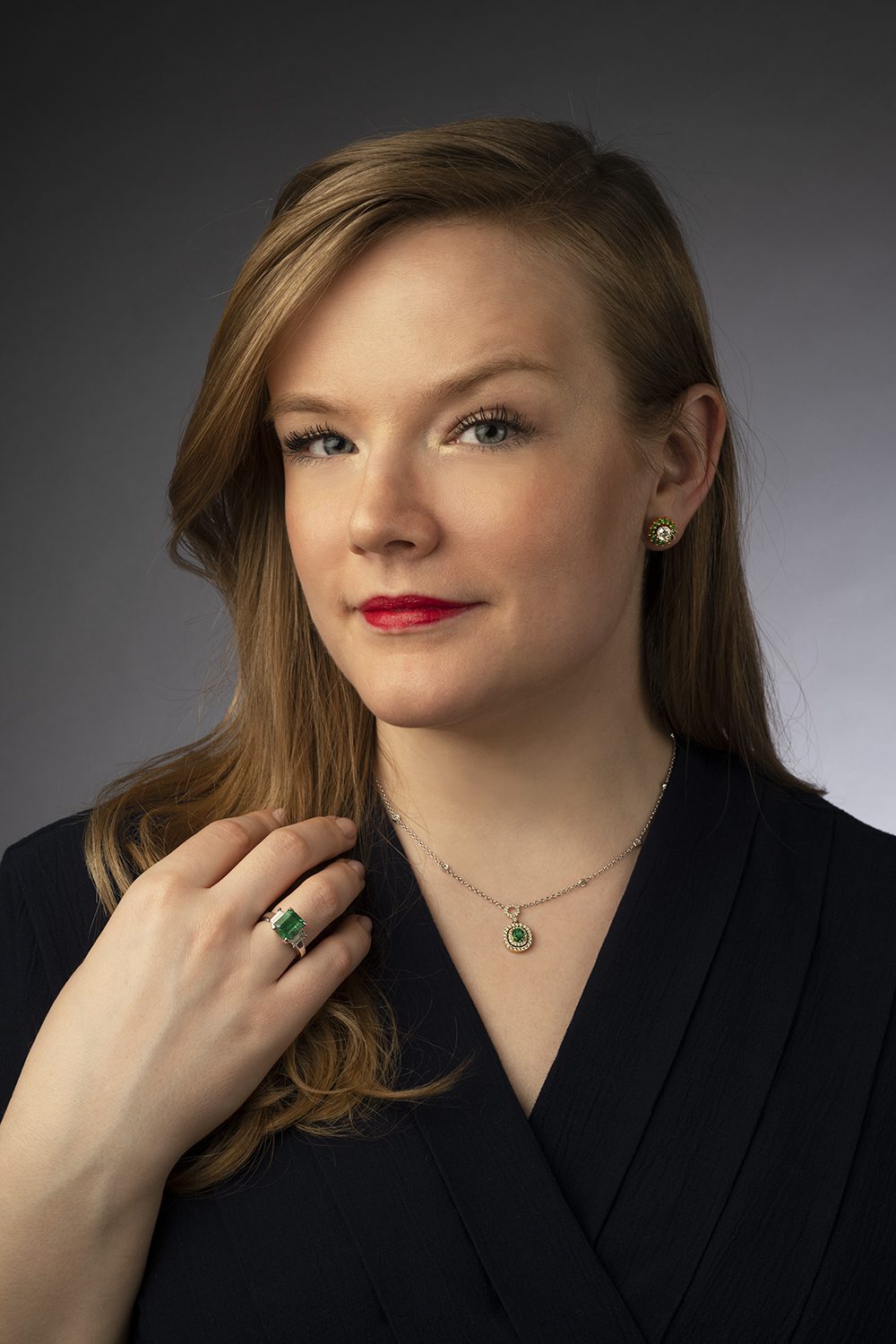 Blonde woman with blonde hair and red lipstick sporting an emerald ring, necklace and earrings